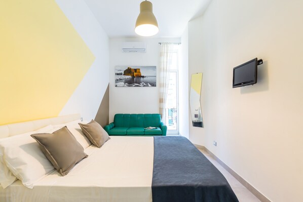 Een hotelkamer met een bed, een groene bank, een flatscreen-tv en een groot raam.