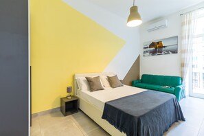 Un dormitorio moderno con una cama, un sofá verde, una mesita de noche y un cuadro en la pared.
