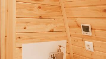 A wooden cabin bathroom with a white sink, a soap dispenser, and a thermostat on the wall.