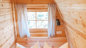Une pièce chaleureuse aménagée dans un chalet en bois, avec deux lits, chacun équipé d’un oreiller et d’une serviette pliée.