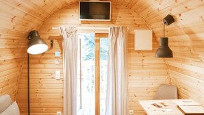 Un chalet confortable aux murs en bois, avec un téléviseur fixé au plafond, un bureau avec une chaise et une grande fenêtre avec des rideaux.