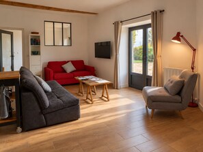 A modern living room with a red sofa, a grey armchair, a wooden coffee table, and a television on the wall.