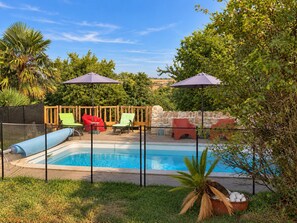 A swimming pool with a stone wall and a wooden fence. There are colorful chairs and umbrellas around the pool.