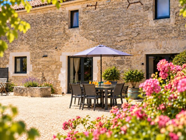 A stone building with a patio area featuring a table and chairs, a potted plant, and a window.