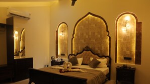 A bedroom with a large bed, a nightstand, a dresser, and a mirror. - Govind Palace Restaurant and Resort (Barwah)