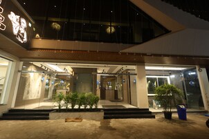 A modern hotel entrance with a glass facade, a wooden overhang, and a potted plant in the foreground.
