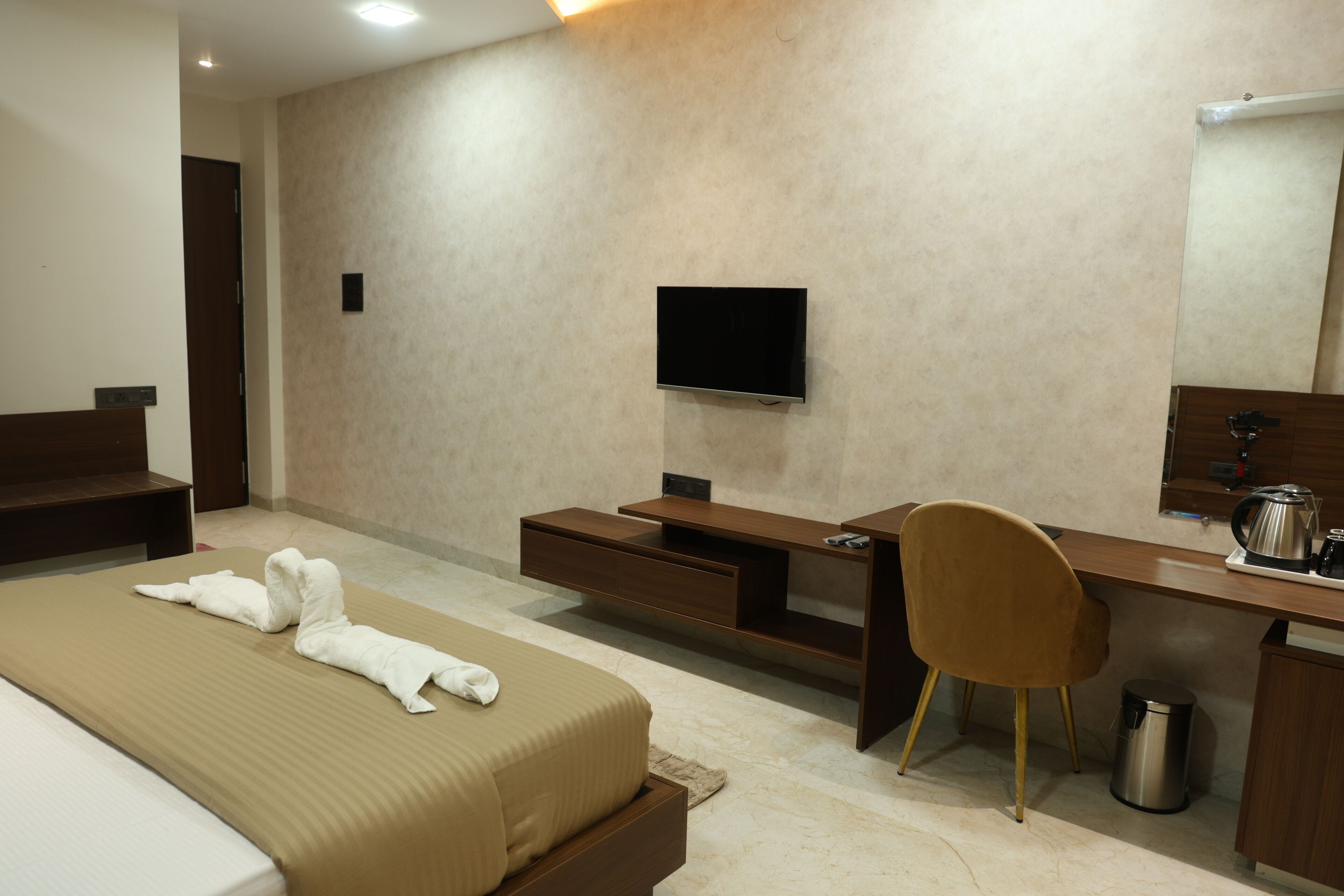 A hotel room with a bed, a desk, a chair, a television, and a small kitchenette area.