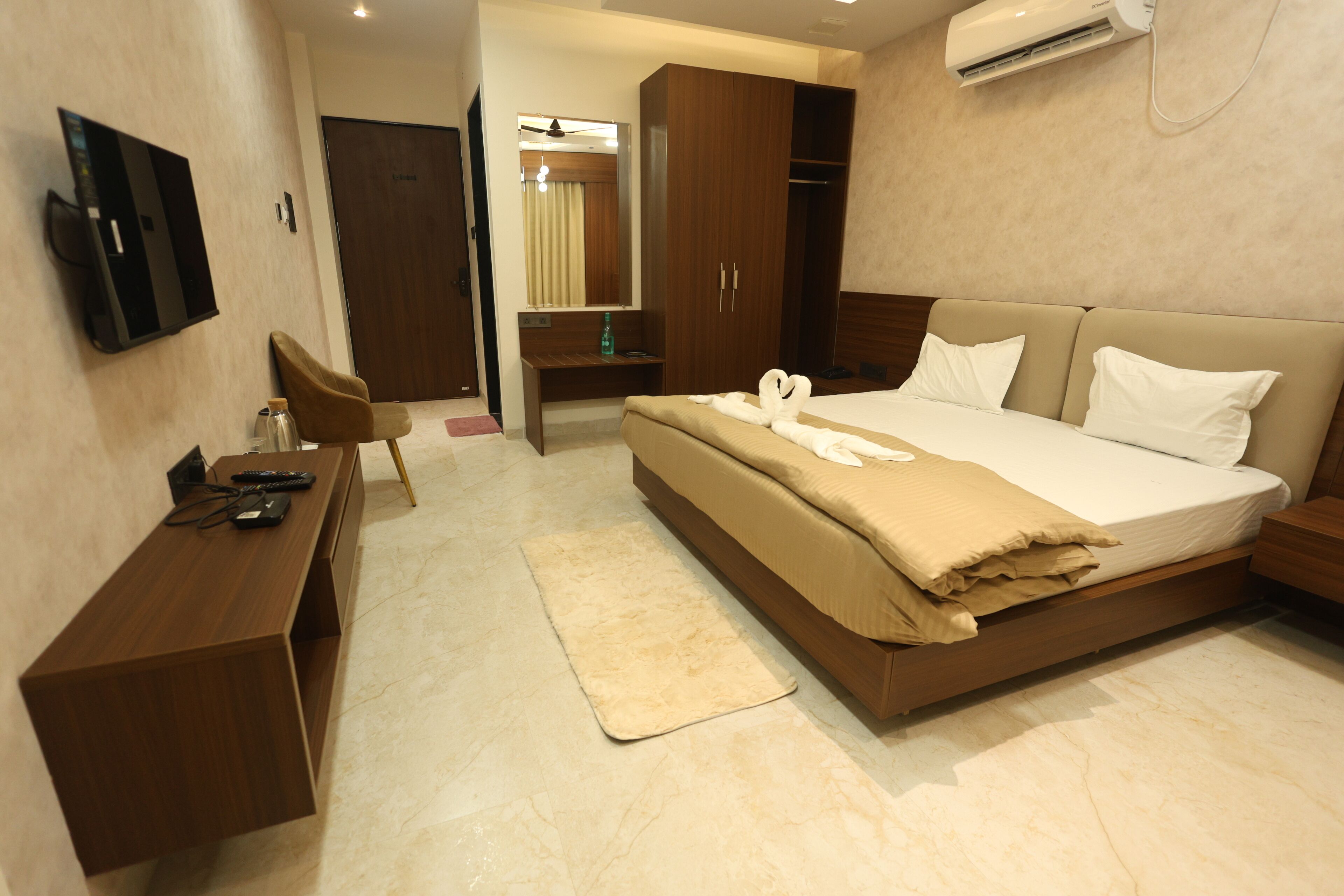 A hotel room with a bed, a desk, a TV, and an air conditioning unit.