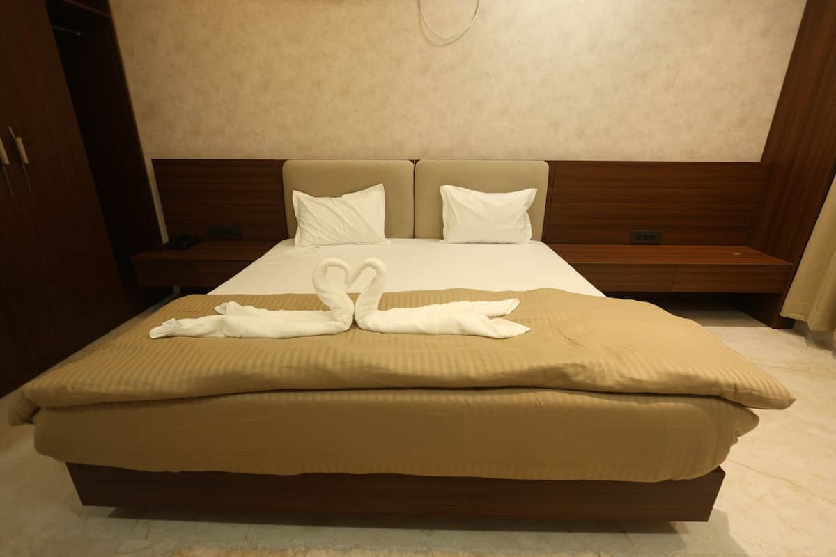 A neatly made bed with two pillows and a pair of towels arranged in a heart shape on the bed.