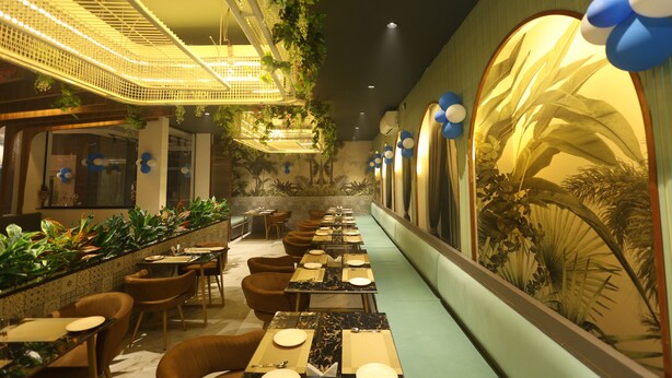 A restaurant with long tables, chairs, and a decorative wall with plants and balloons. - Govind Palace Restaurant and Resort (Barwah)