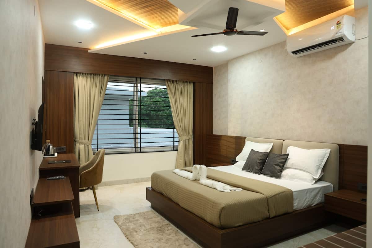 A modern hotel room with a large bed, a desk, and a chair. There is a window with curtains, a ceiling fan, and an air conditioning unit.