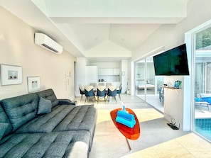 Una sala de estar moderna con sofá, comedor con sillas, televisor y vista a la piscina.