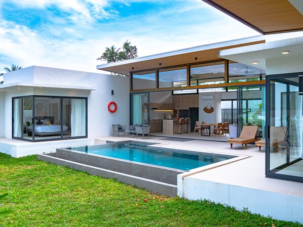 A modern house with a swimming pool, glass doors, and a dining area.