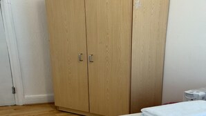 A bedroom with a wooden wardrobe, a radiator, and a neatly folded white towel on the bed.