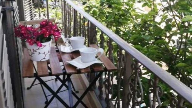 Un balcón con una mesa y sillas de madera, una planta en maceta y una escalera.
