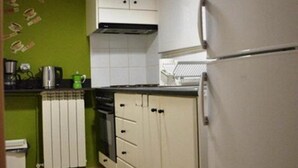 Una cocina compacta con armarios blancos, un refrigerador y una pared verde.