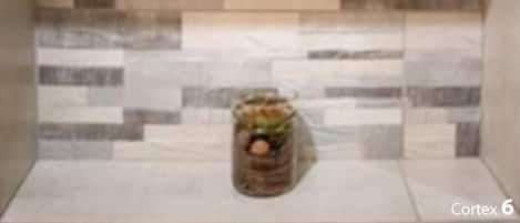 Et badeværelse med flisebeklædt bagvæg, hylde med toiletartikler og en lille plante.