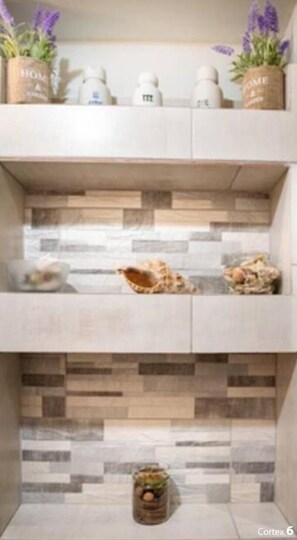 A bathroom with a tiled backsplash, a shelf with toiletries, and a small plant.