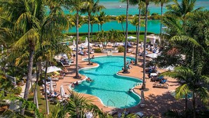 Ein Poolbereich eines Resorts mit mehreren Schwimmbecken, umgeben von Palmen und Liegestühlen.