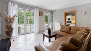A living room with a sofa, a coffee table, a potted plant, and a view through glass doors to an outdoor area. - Apartment 'Am Wasser 2' with Lake View, Shared Terrace, and Wi-Fi (Groß Lindow)