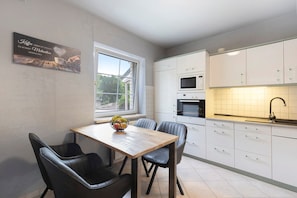 Une cuisine moderne avec des meubles blancs, une table à manger en bois et une chaise noire.