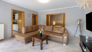 A living room with a brown leather sofa, a wooden coffee table with a vase of flowers, a television, and a tripod. - Apartment 'Am Wasser 2' with Lake View, Shared Terrace, and Wi-Fi (Groß Lindow)