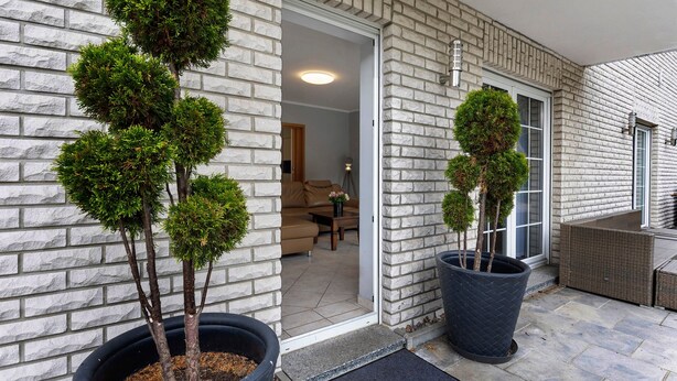 A modern building with a brick exterior, a door leading to an interior space, and potted trees. - Apartment 'Am Wasser 2' with Lake View, Shared Terrace, and Wi-Fi (Groß Lindow)