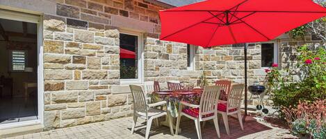 A stone building with a patio area featuring a table and chairs under a red umbrella.