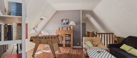 Ein gemütliches Schlafzimmer im Loft-Stil mit Holzbalkendecke, einem Kicker, einem Bücherregal, einer Couch und einem Schreibtisch.