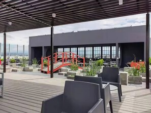 A rooftop terrace with outdoor seating, a red bridge, and a view of the cityscape. - Luxury Loft in San Jose CR (San José)
