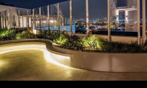 A nighttime view of a rooftop terrace with a curved pool, plants, and a cityscape in the background. - Luxury Loft in San Jose CR (San José)