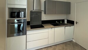 A modern kitchen with white cabinetry, a built-in oven, a microwave, a gas stove, and a stainless steel range hood. - Charmant appartement Nancy centre (Nancy)