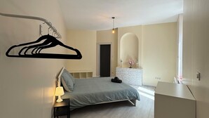 A bedroom with a bed, bedside table, lamp, hanging clothes rack, and a dresser. - Charmant appartement Nancy centre (Nancy)