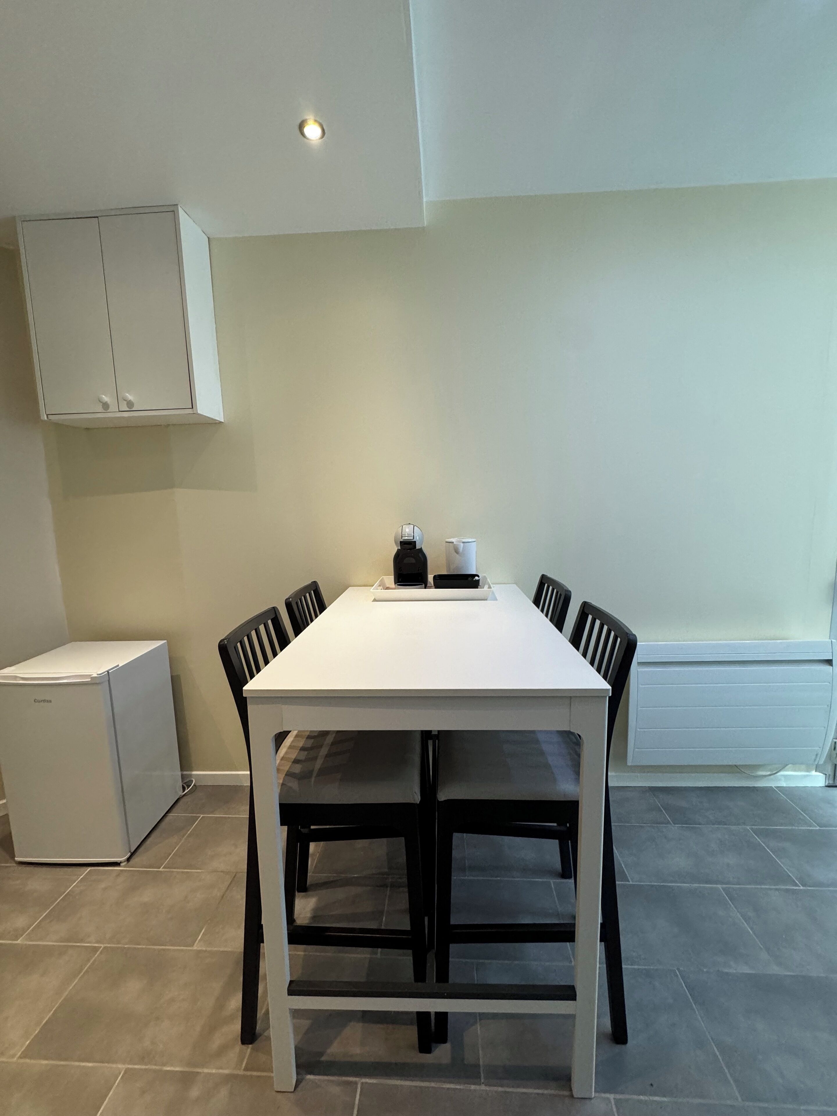 Une cuisine moderne avec une table blanche, des chaises noires, un réfrigérateur blanc et un meuble blanc.