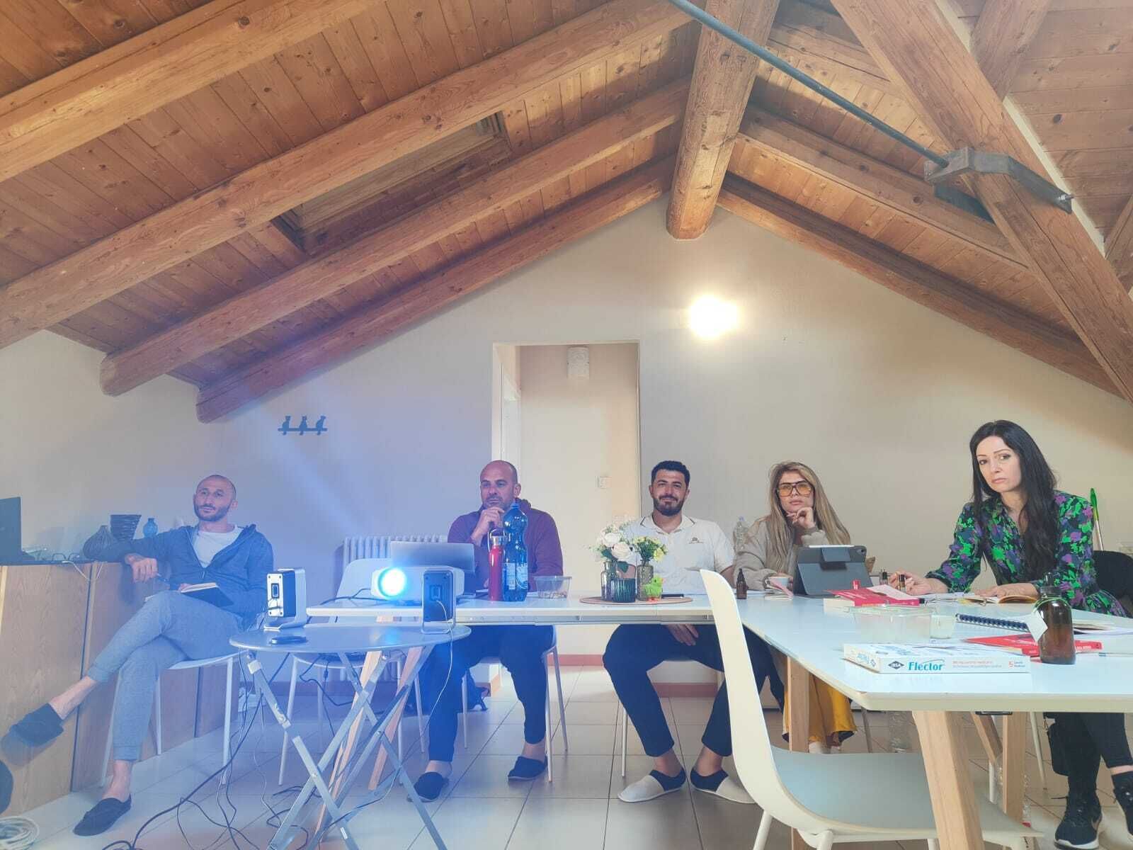 A group of people in a room with wooden beams on the ceiling, a whiteboard, and a table with laptops and papers.