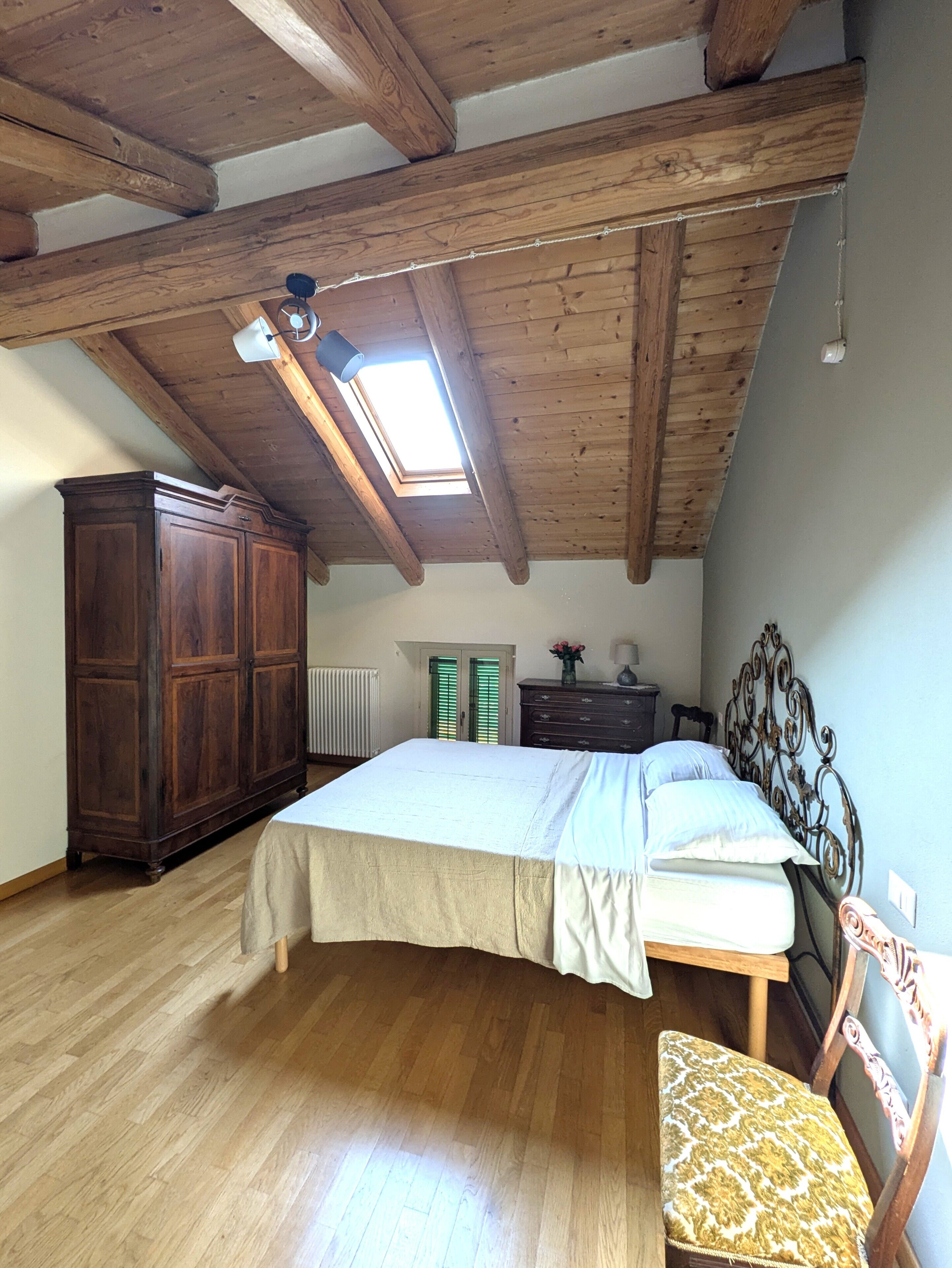 Ein Schlafzimmer mit schrägem Dach, einem Bett, einem Kleiderschrank, einem Heizkörper und einem Fenster.