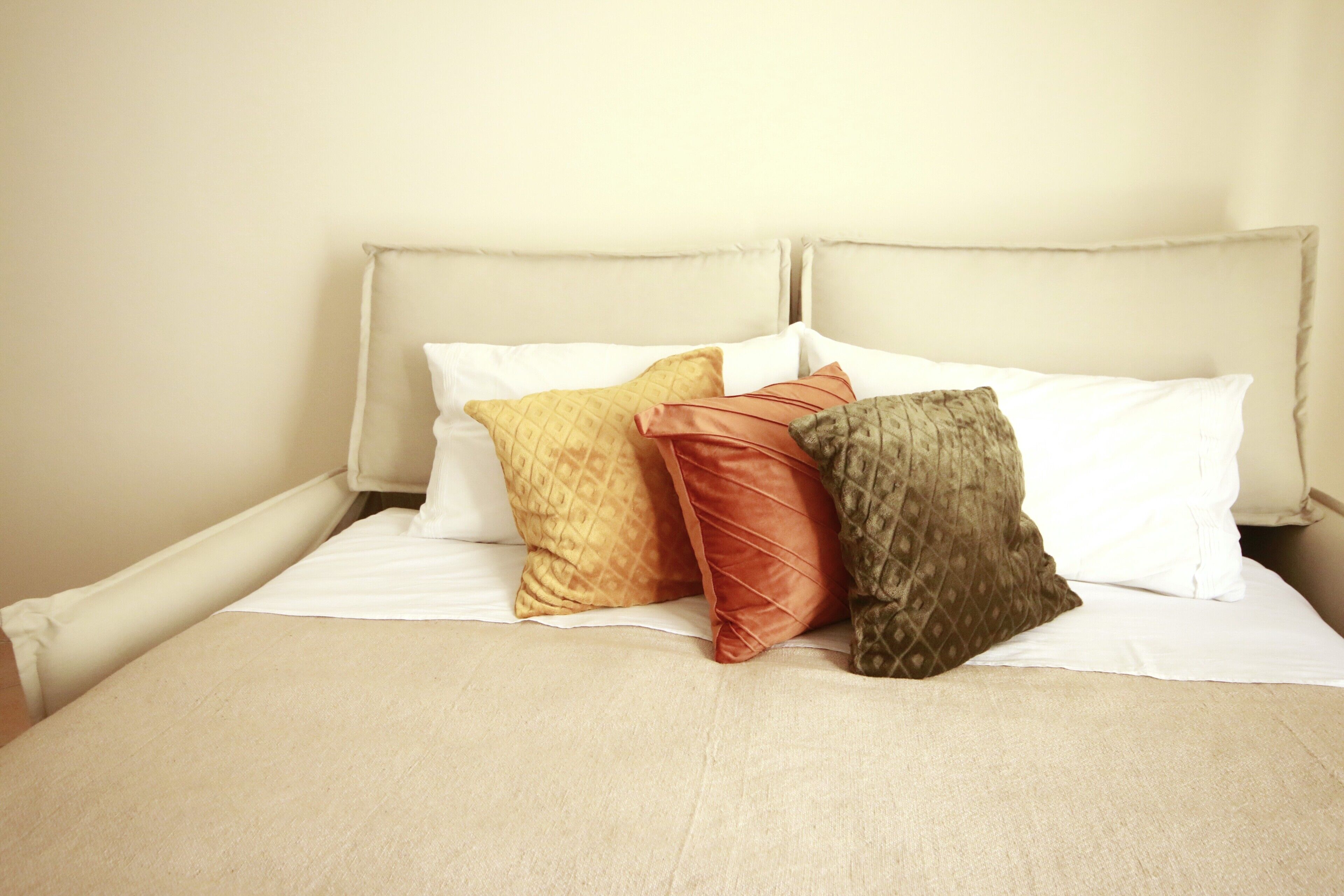 Ein Bett mit beigem Kopfteil und weißer Bettwäsche.