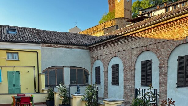 A courtyard with outdoor seating, a clock tower, and a building with arched windows. - Private historic house for groups with terrace 24 guests 6 apartments Monferrato (Viarigi)