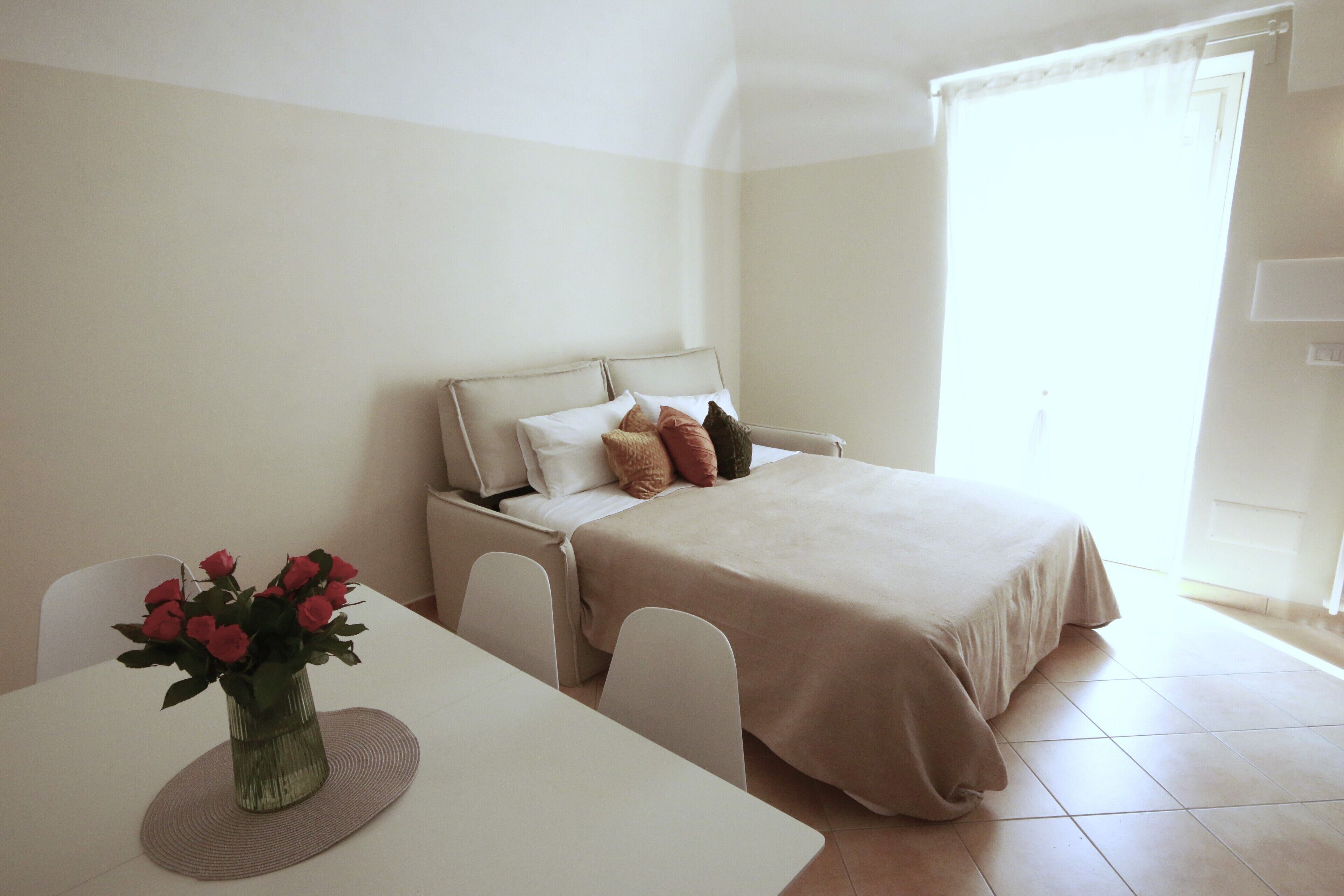 A bedroom with a bed, bedside table, and a vase of flowers.