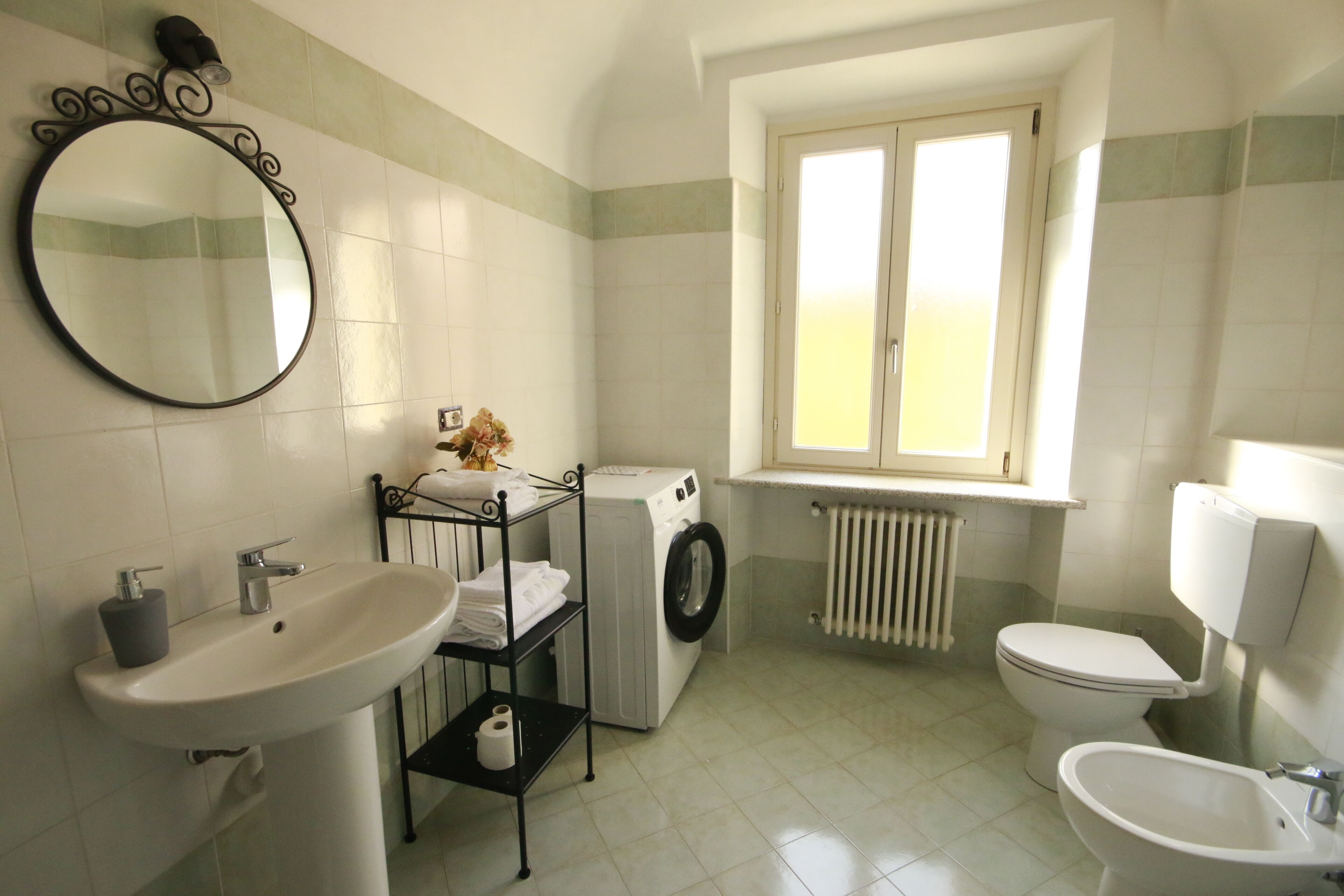 A bathroom with a sink, mirror, washing machine, toilet, and bidet.