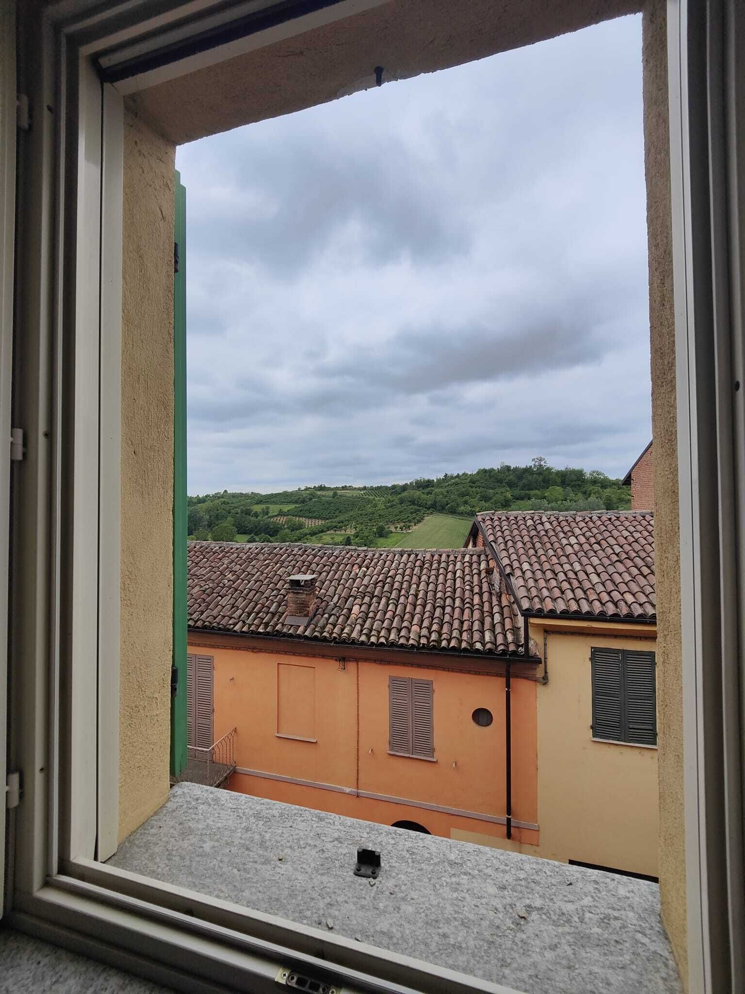 A window view of terracotta-roofed buildings, a clear sky, and a green landscape.