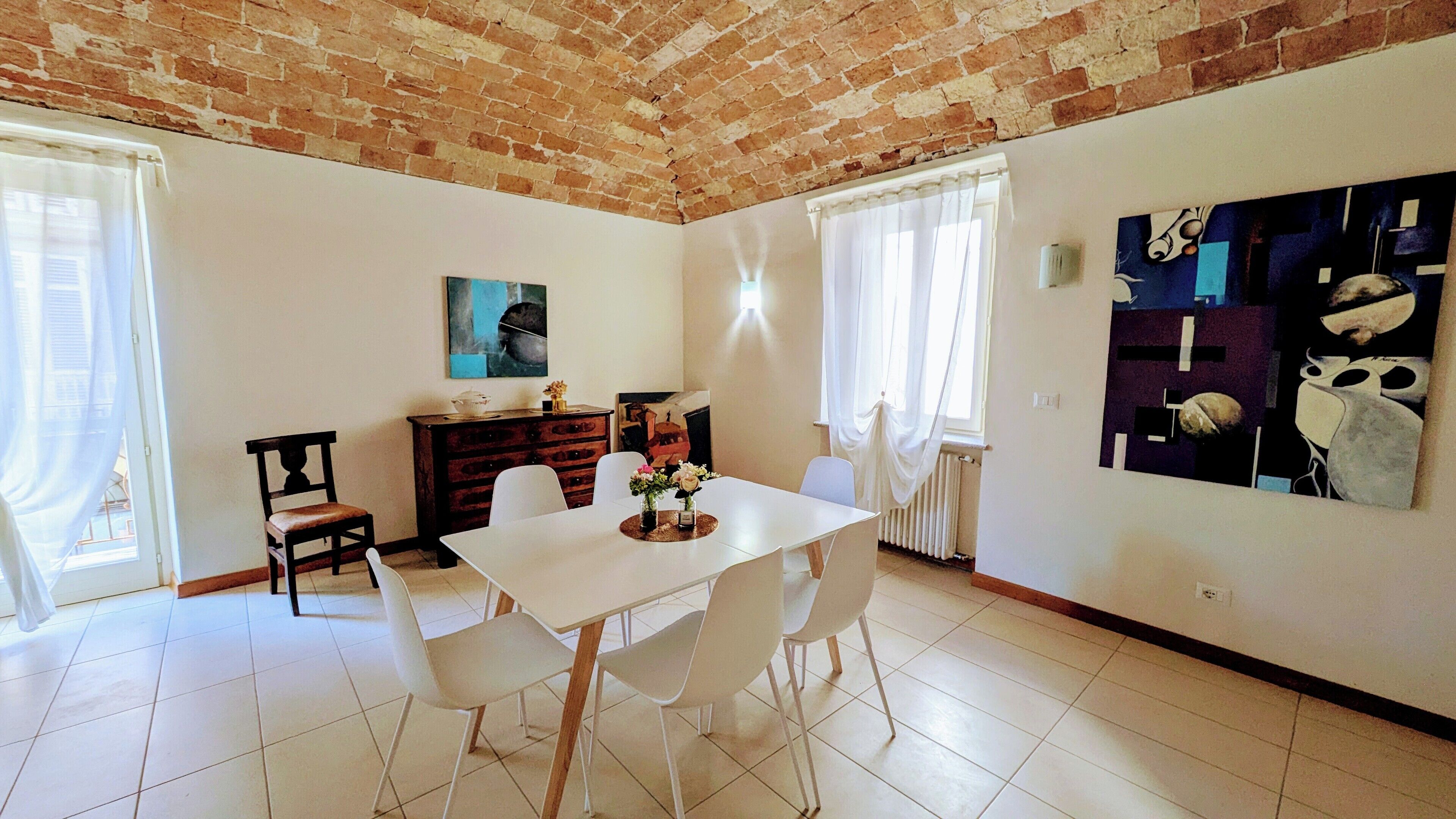Un coin repas avec une table et des chaises blanches, un meuble en bois et un tableau accroché au mur.