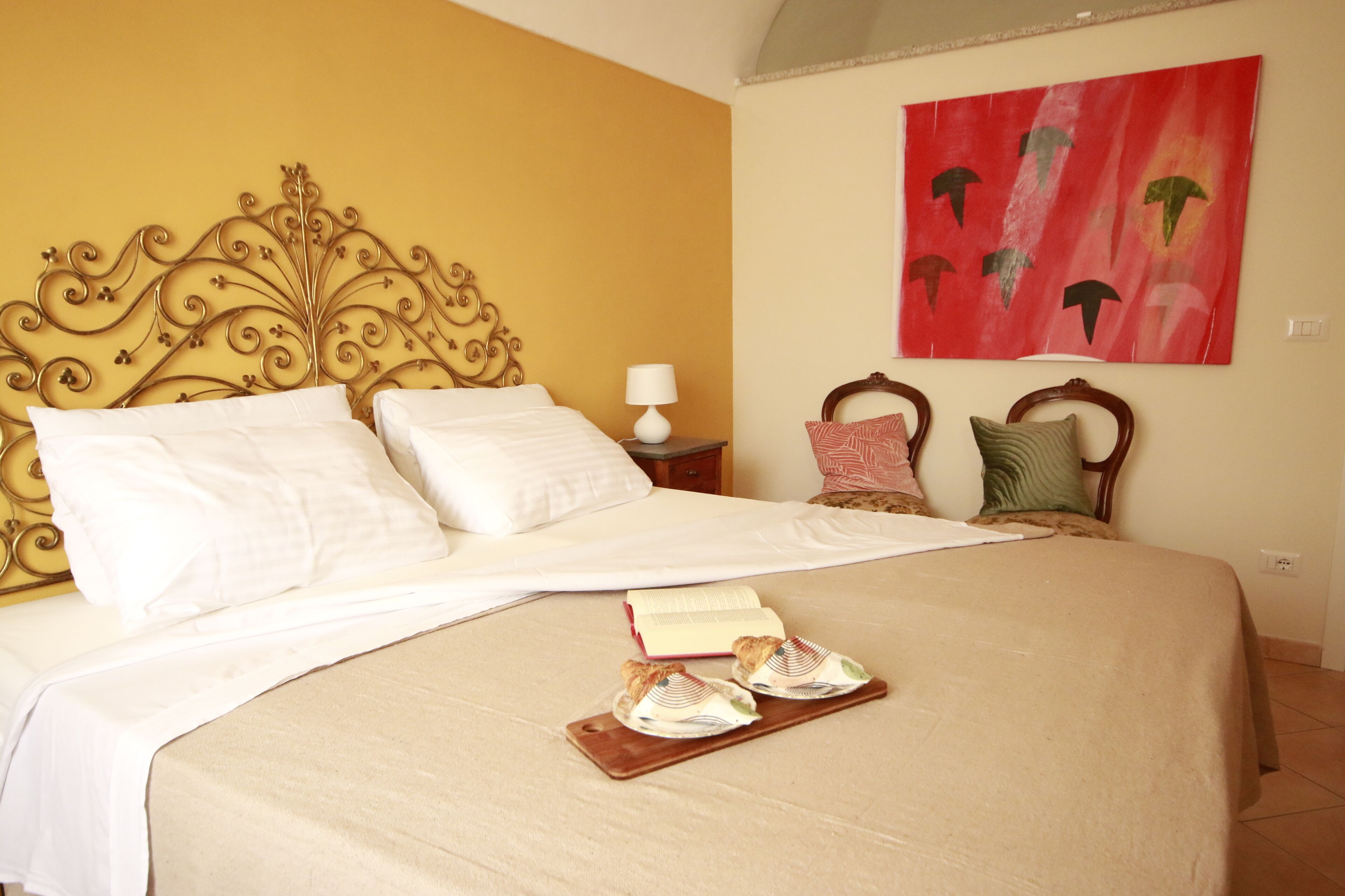 Un lit bien fait, avec du linge de lit blanc, une tête de lit décorative et un tableau abstrait rouge accroché au mur.