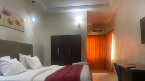 A hotel room with a bed, a desk, a wardrobe, and a shower area. - Stanzel Grand Resort (Abuja)