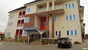 A multi-story building with a covered entrance, balconies, and a car parked in front. - Stanzel Grand Resort (Abuja)
