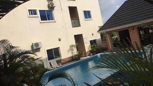 A building with multiple windows, a swimming pool, and some potted plants. - Stanzel Grand Resort (Abuja)