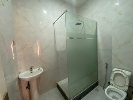 Un baño con ducha de vidrio, lavamanos sobre pedestal y retrete.