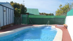 Une piscine bordée de carreaux aux motifs géométriques, entourée d’une terrasse rouge et d’une clôture verte.