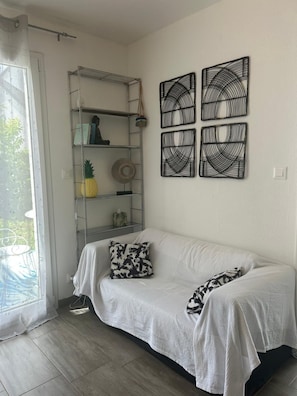 A room with a white sofa, a metal shelving unit, and three wall-mounted decorative items. - Charming House in Bale-Leymen—Your Perfect Home for Pets (Leymen)