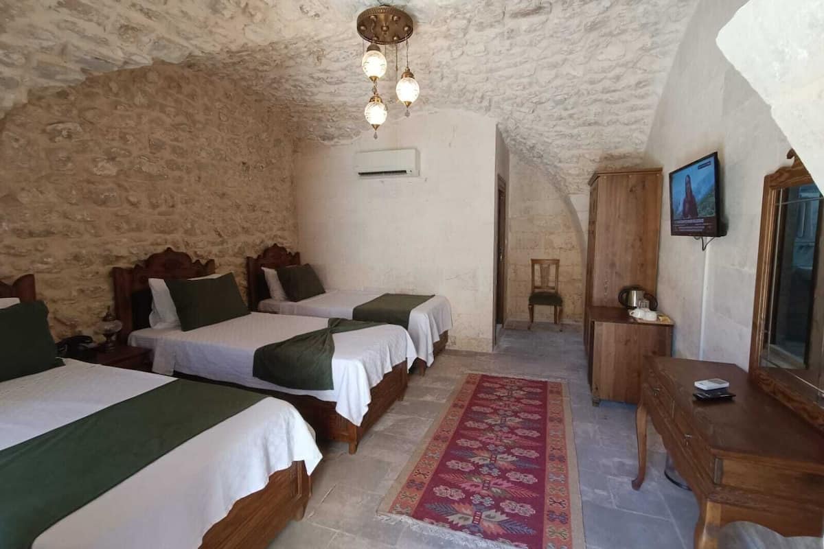 A rustic room with three wooden beds, a stone ceiling, a wooden cabinet, and a television.